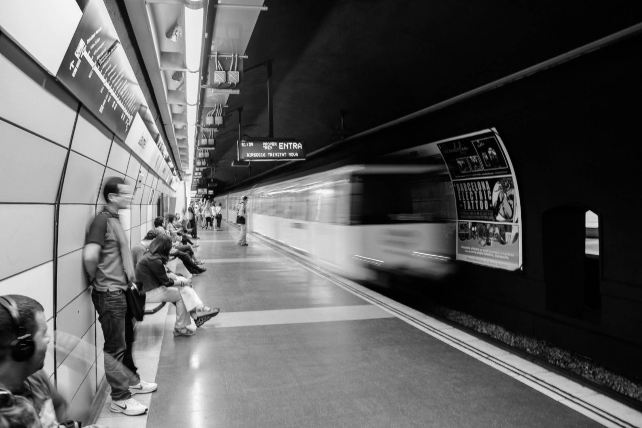 Black and white photograph of passengers waiting as a train blurs through an underground station