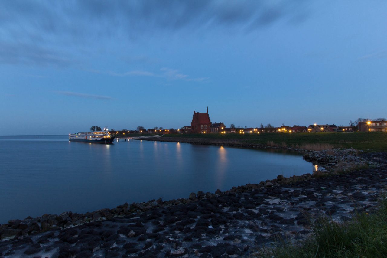 A town on the shoreline at blue hour, seen across a rocky bay
