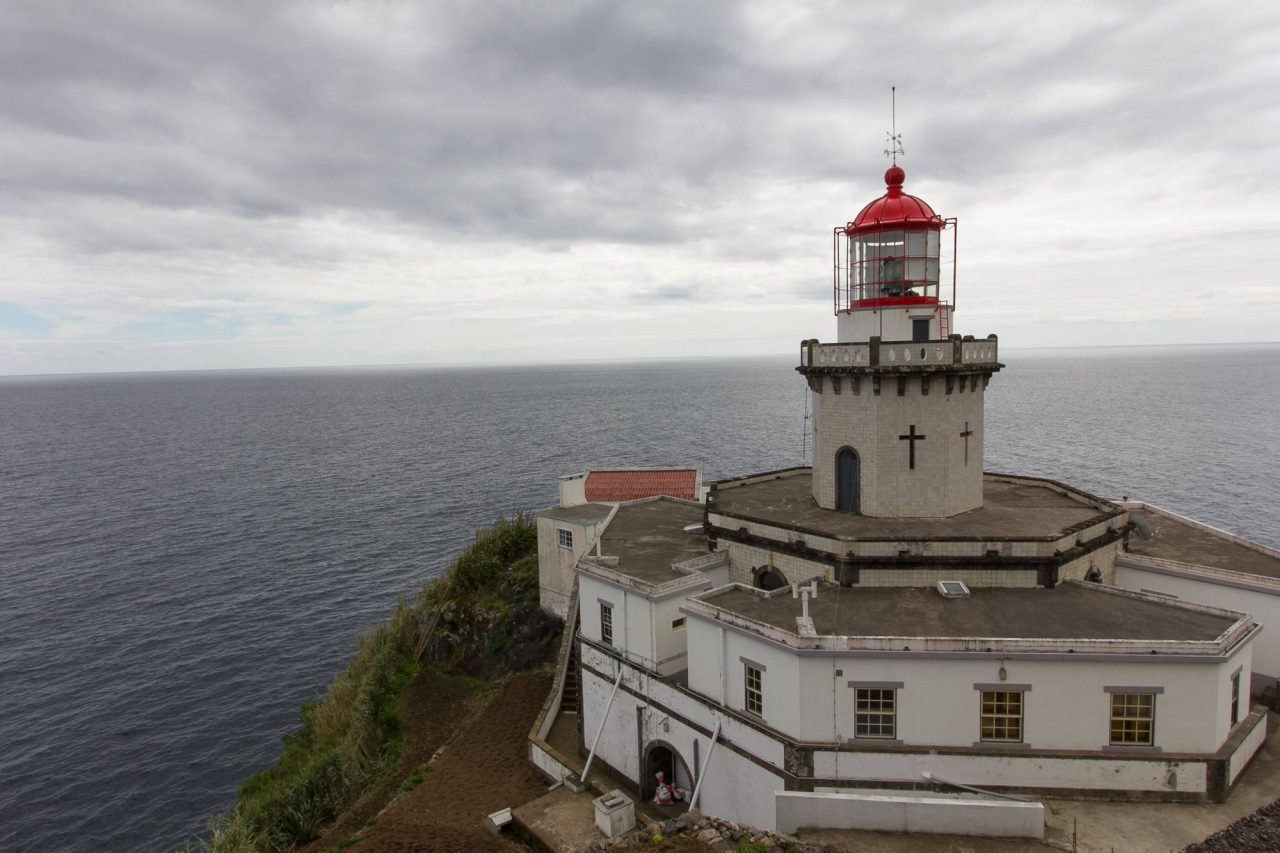 A white lighthouse with a red lantern seen from above, the ocean beyond