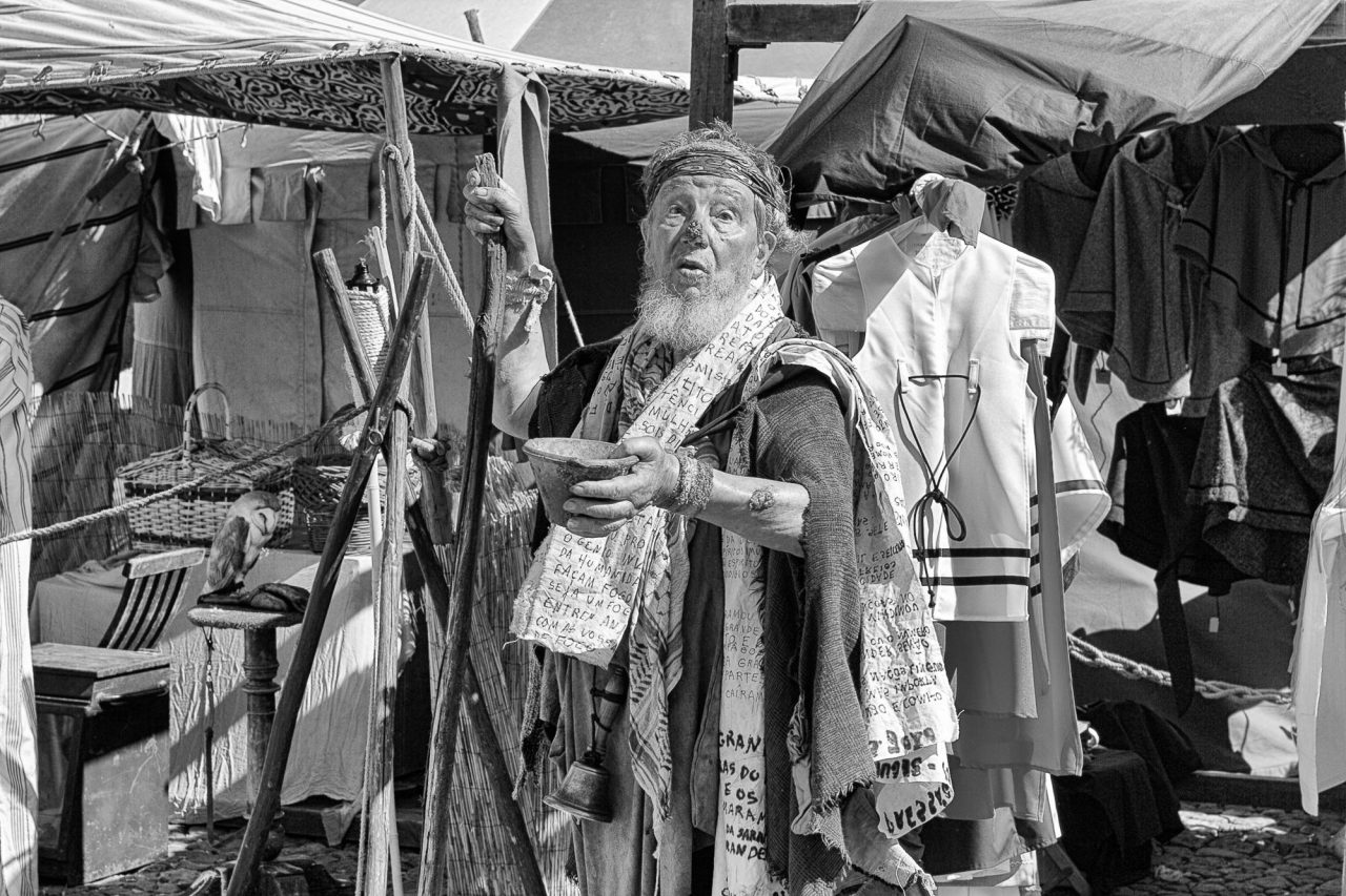 Black and white photograph of a man among clothes hanging at a street market stall