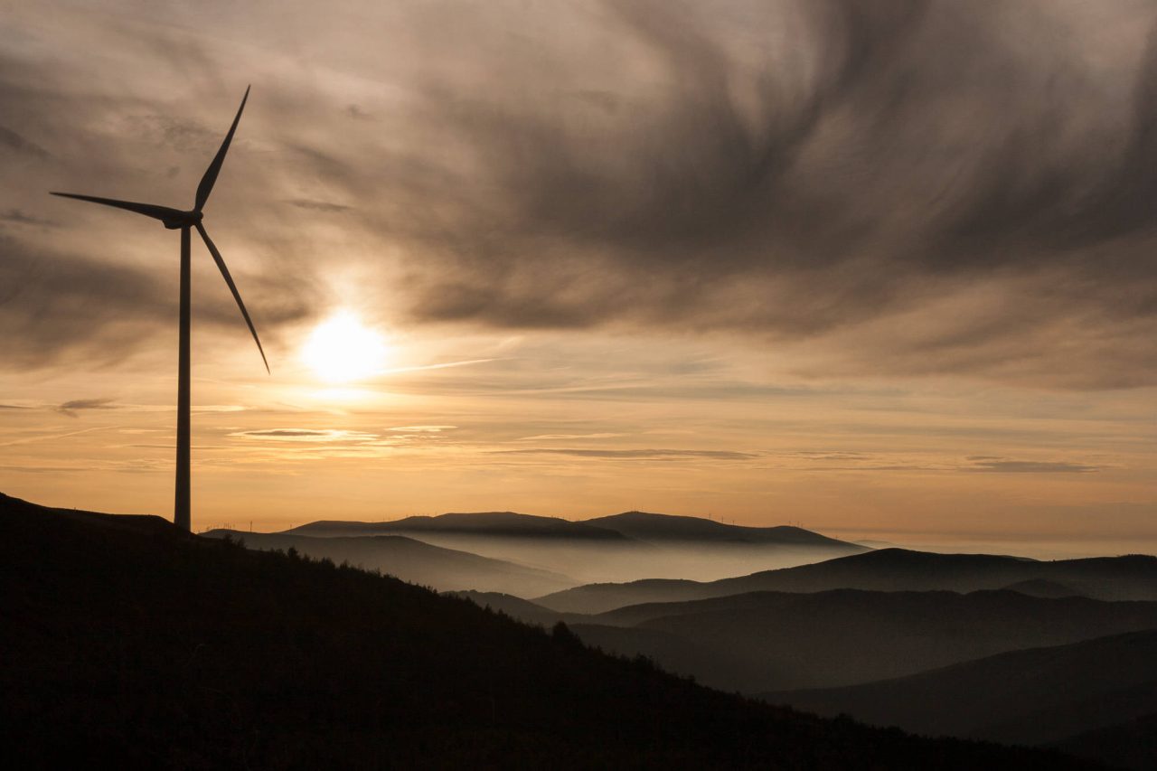 A single wind turbine against the setting sun above layered hills